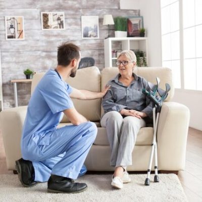 male-health-visitor-nursing-home-talking-with-retired-old-woman-while-sitting-couch-old-woman-with-crutches_482257-45110